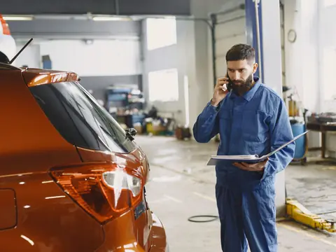 A technician on the phone with a binder beside an orange SUV in the shop