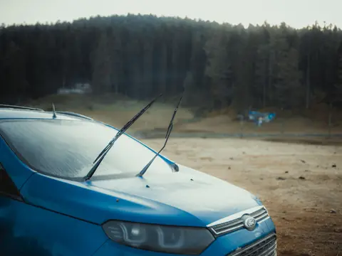 A blue SUV with its wipers raised off a frosted windshield